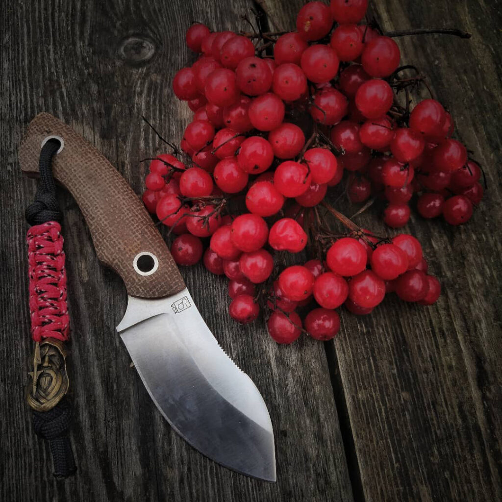 Ein Messer mit roten Beeren auf einem Holztisch.
