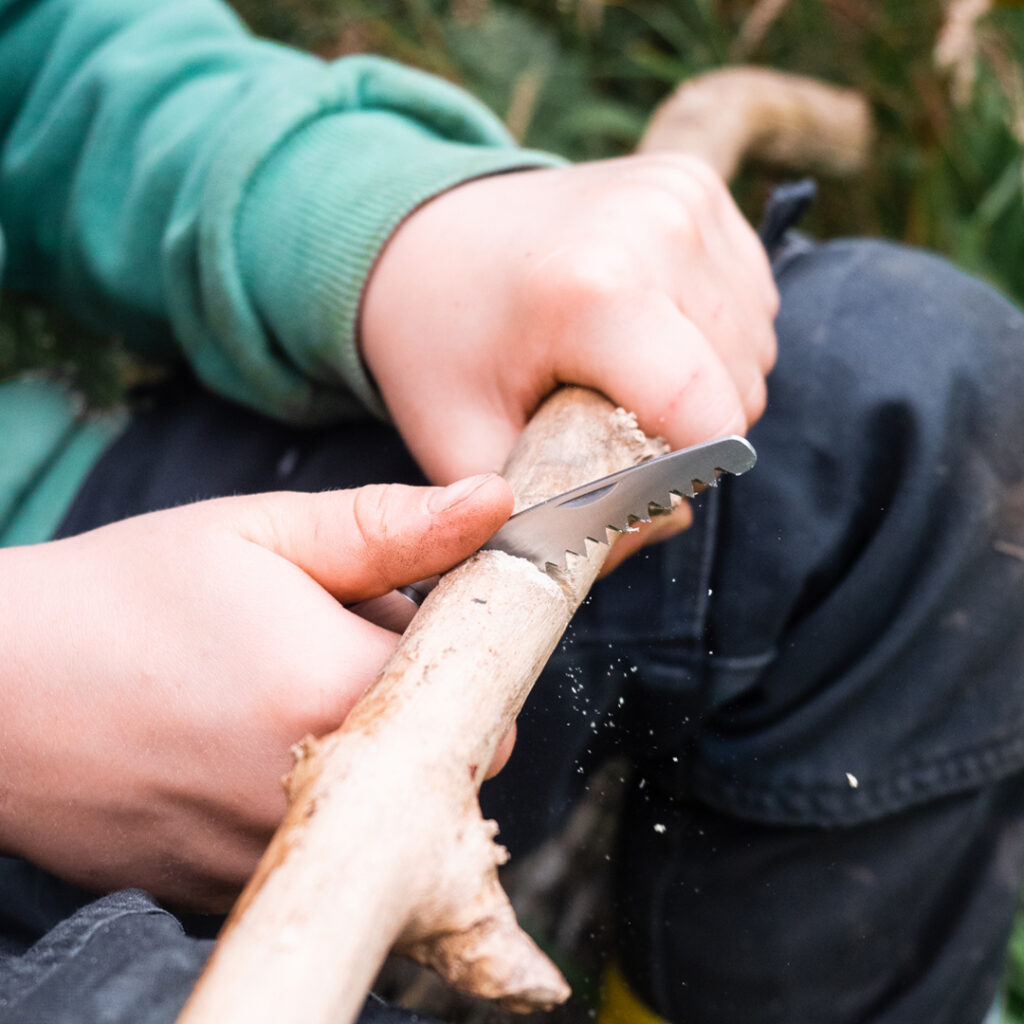 Ein Kind schneidet mit einem Messer ein Stück Holz.