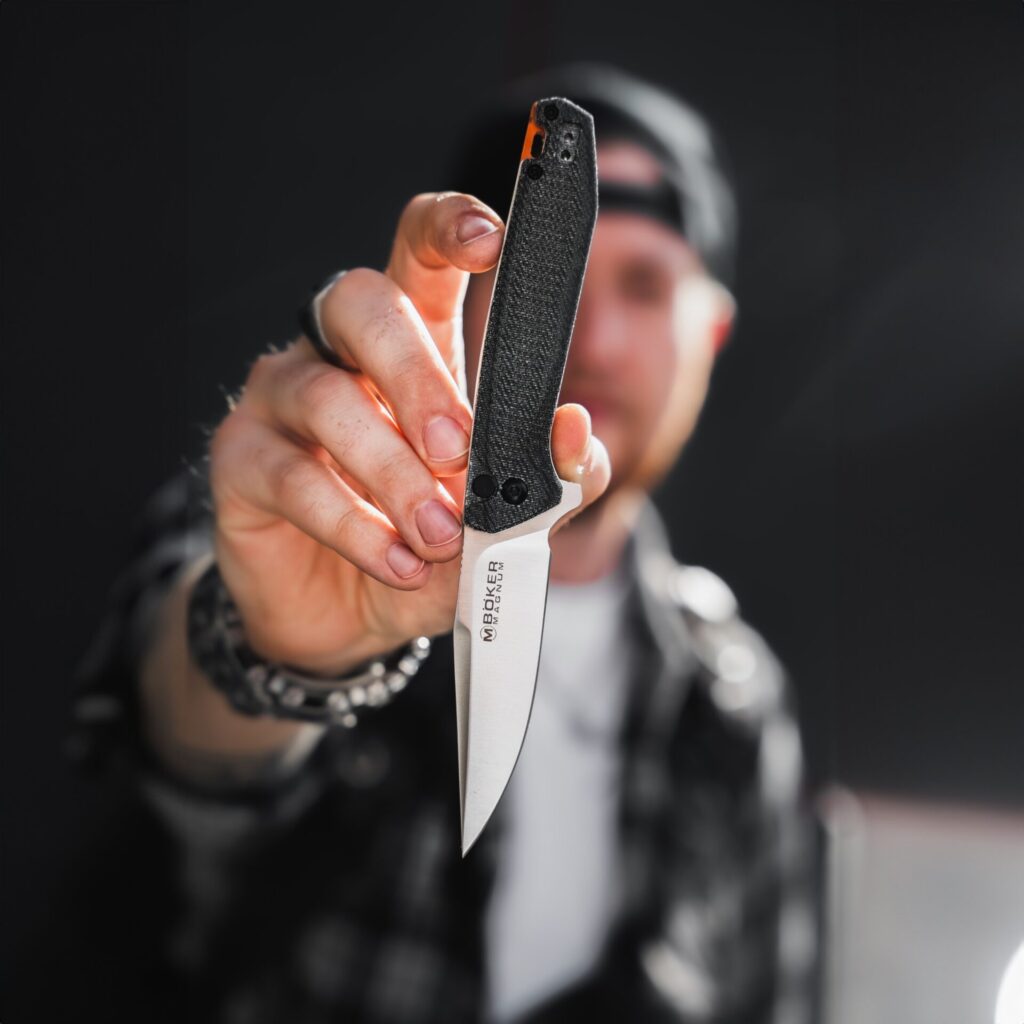 Ein Mann hält ein Messer vor einem dunklen Hintergrund hoch.